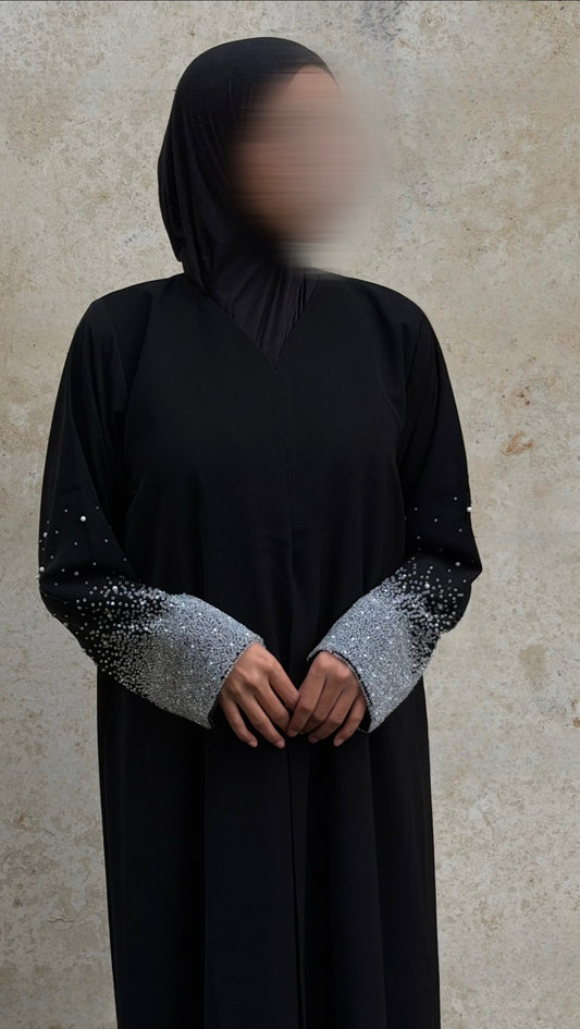 Person wearing a black abaya with silver embellishments on a beige background